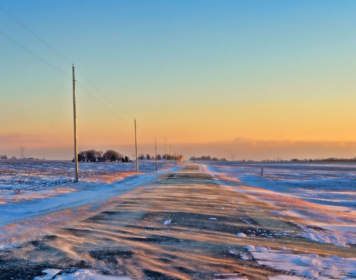 Windblown snow on a country road near sunset